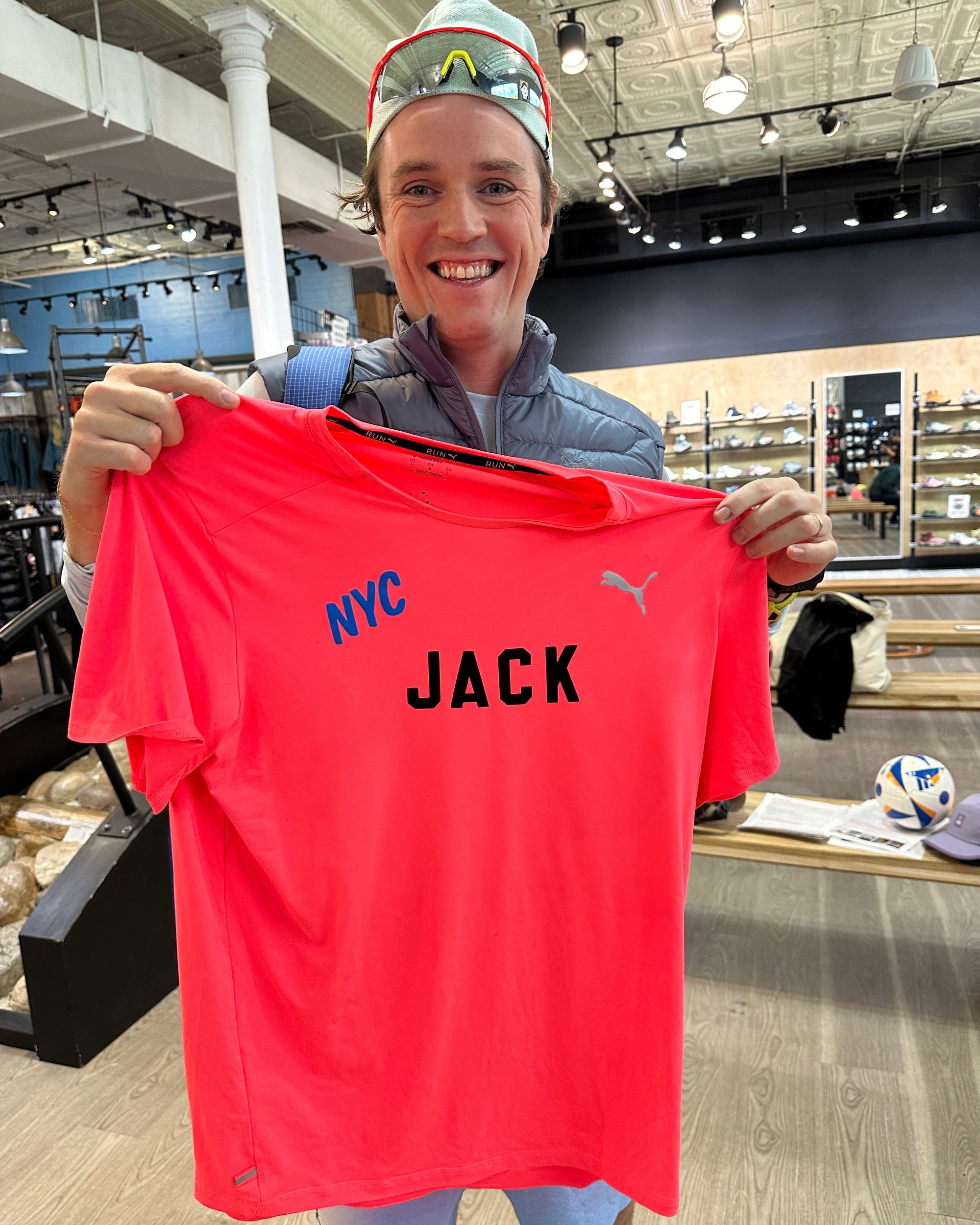 Jack Coyne holding a red shirt with 'NYC JACK' text in an indoor setting