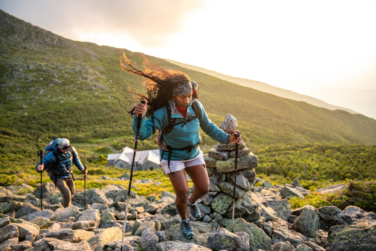 Two hikers on a rocky trail with mountains in the background photo by Osprey
