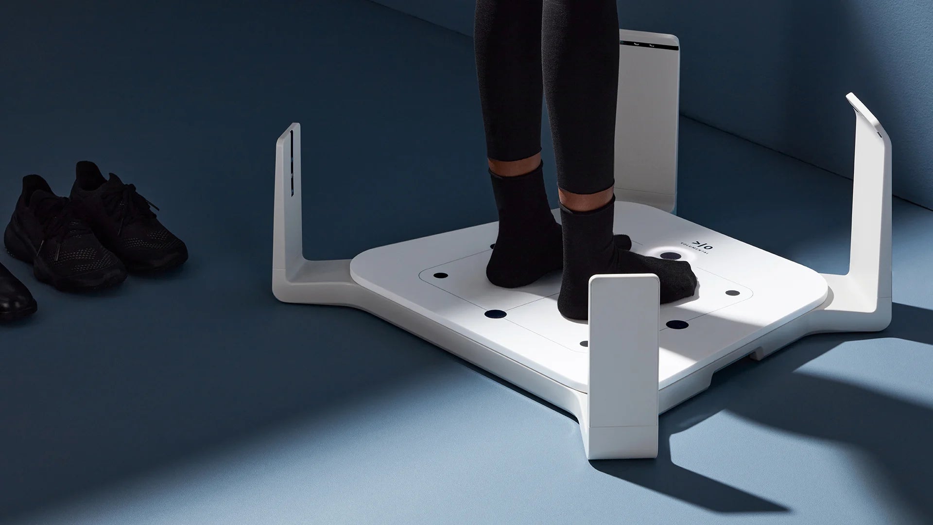 Person using a volumental foot scanner on a blue floor with shoes nearby for gait analysis photo by volumental