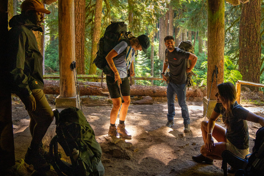 Group of hikers in a forest setting with backpacks and outdoor gear. Photo by Fjallraven