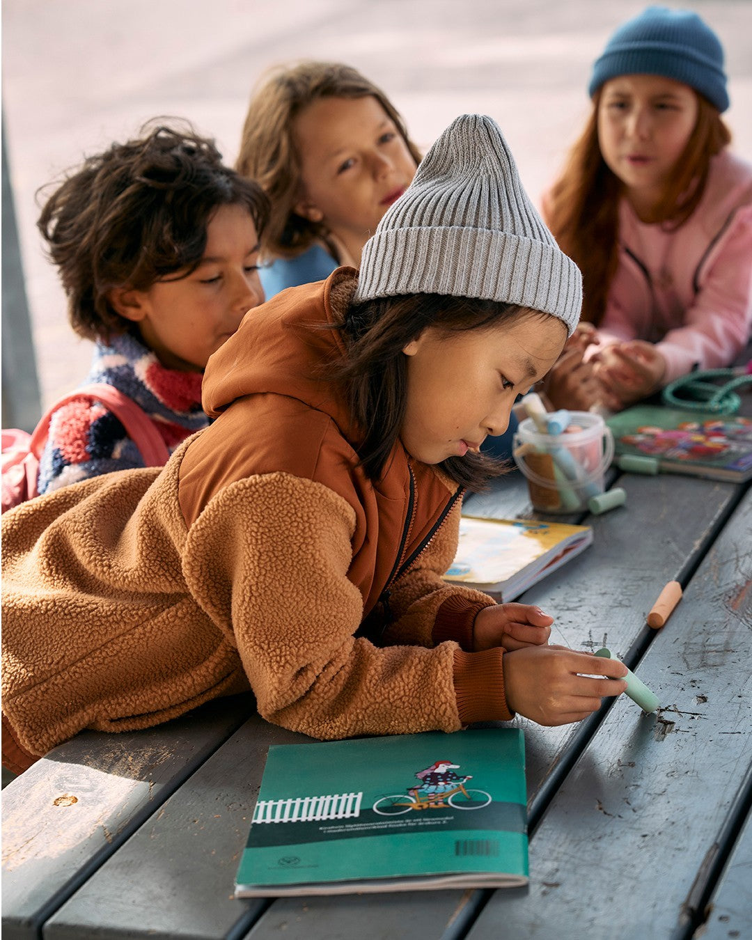 Children sitting outdoors, with one child writing in a notebook. wearing Reima photo by Reima