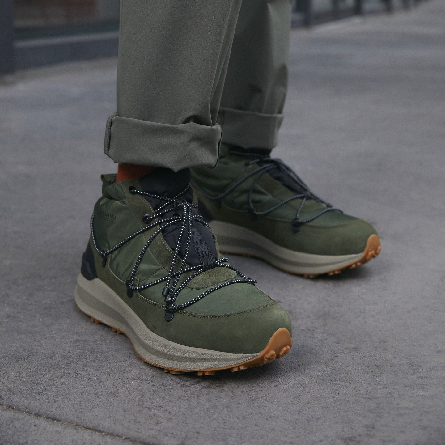 Green hiking shoes with brown soles worn by a person on a blurred street background Photo by Pajar