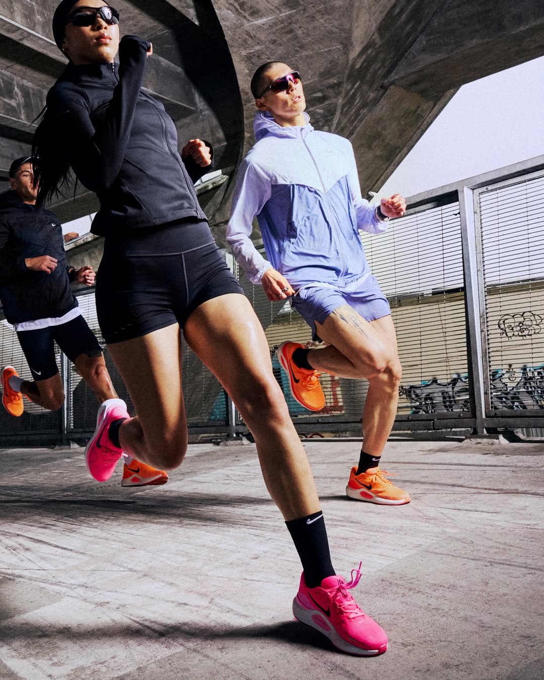 Three people running outdoors on a concrete surface with graffiti in the background