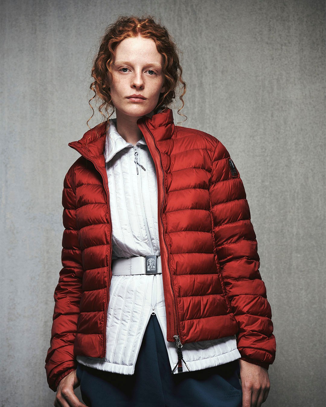 Person wearing a red puffer jacket on a gray background photo by Parajumpers