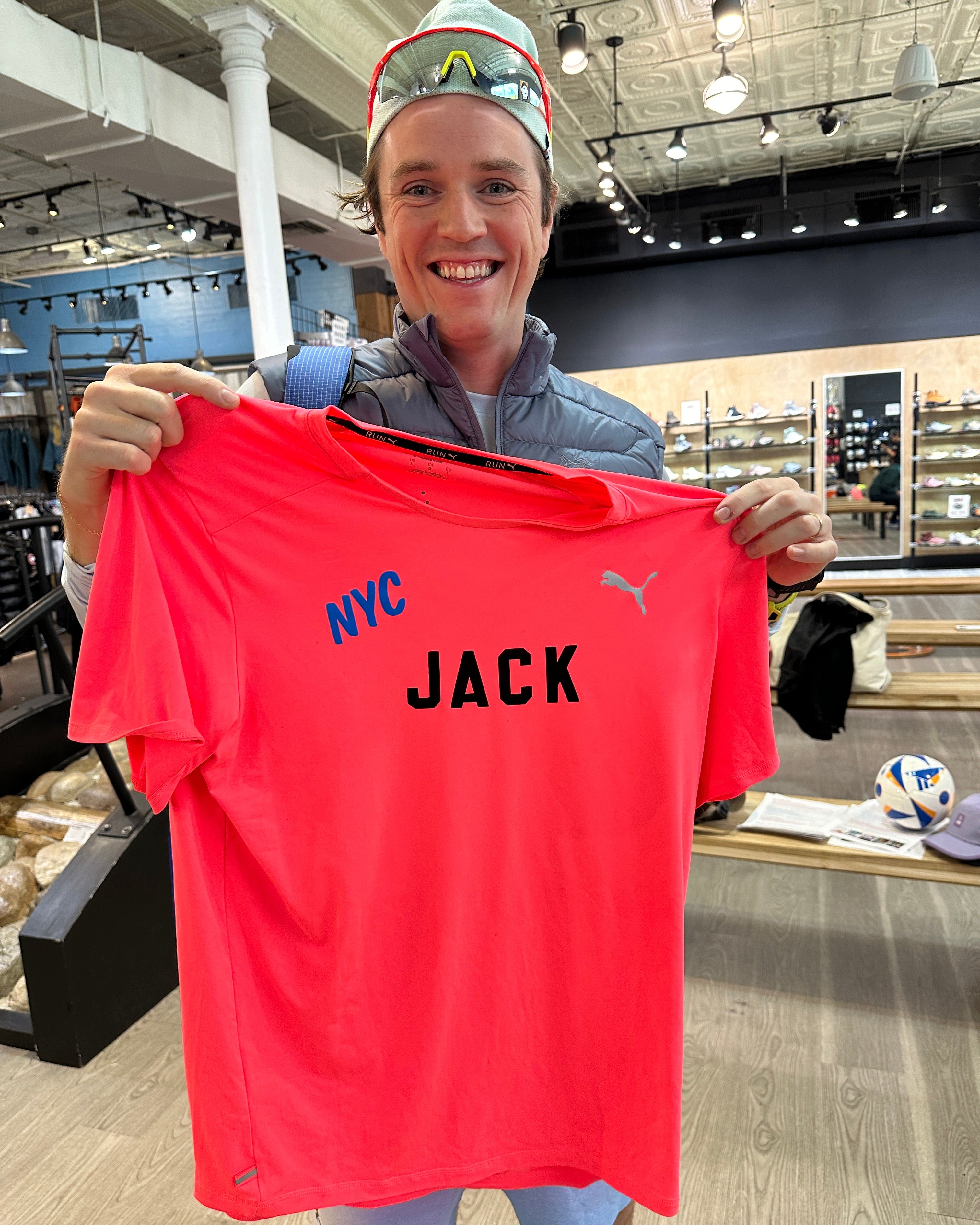 Jack Coyne holding a red shirt with 'NYC JACK' text in an indoor setting