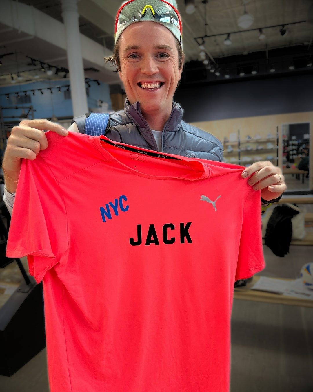 Person holding a red shirt with 'NYC JACK' printed on it, indoors.