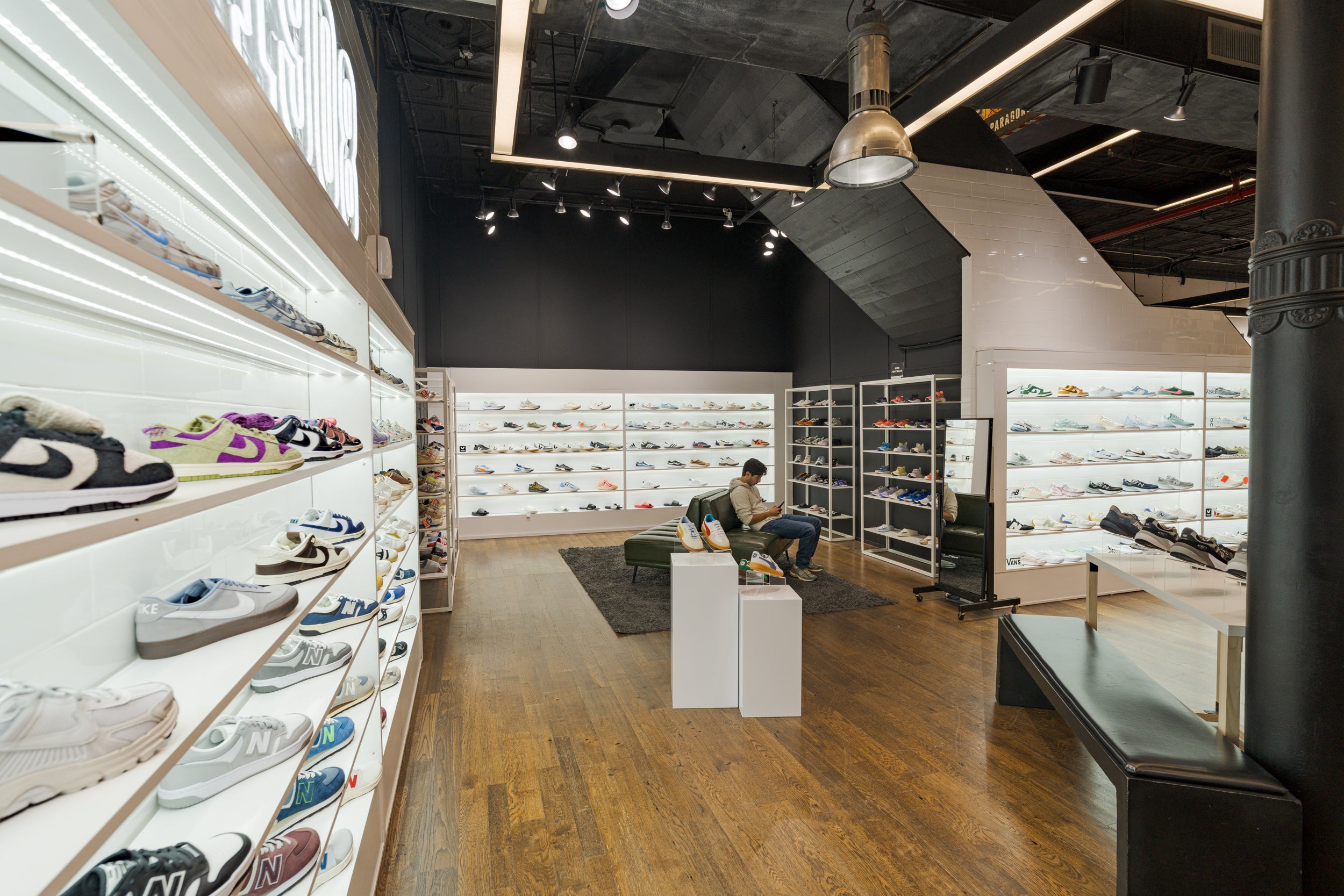 Modern shoe store interior with shelves displaying various shoes and a person sitting on a bench.