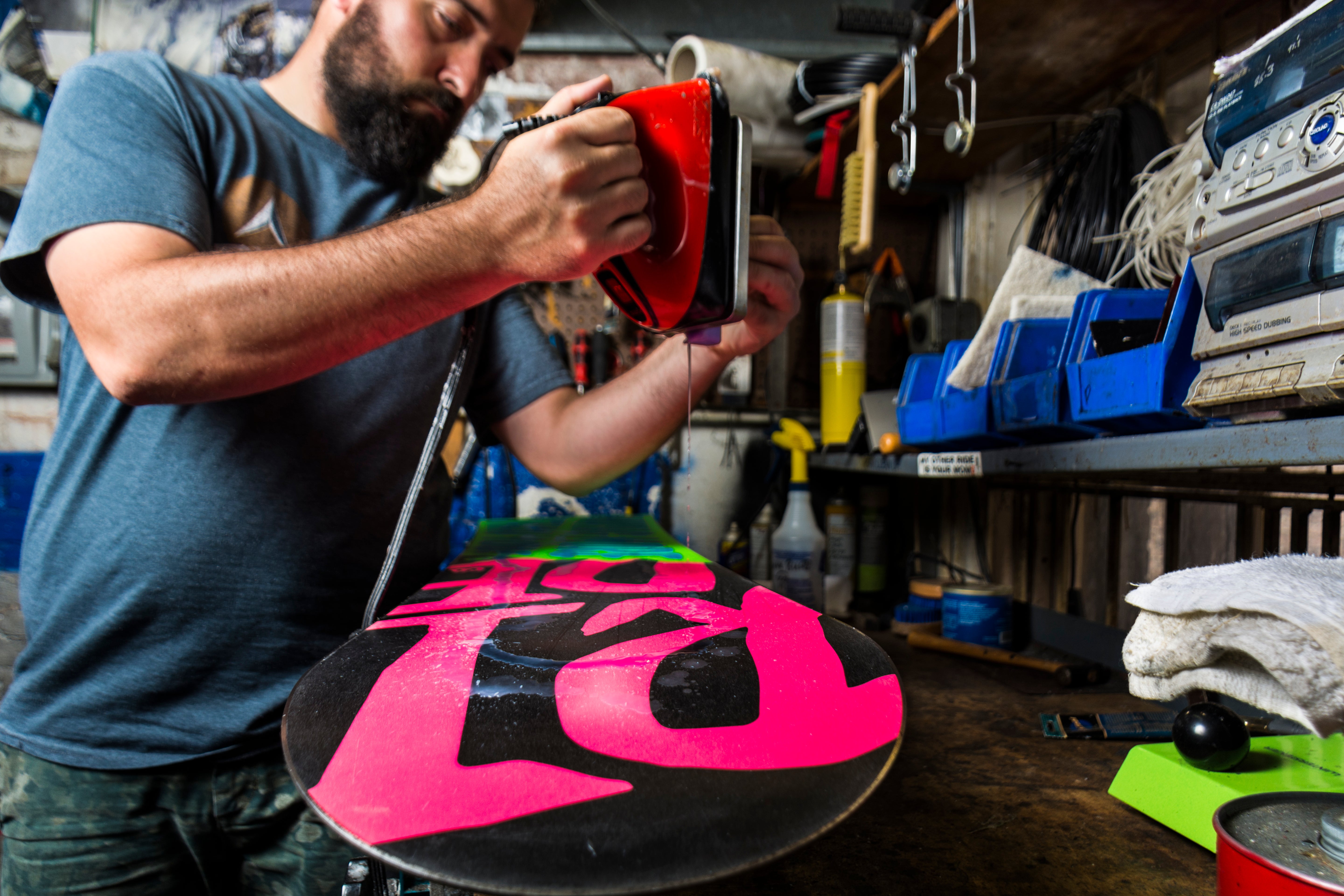 Man working on a colorful snowboard in a workshop.