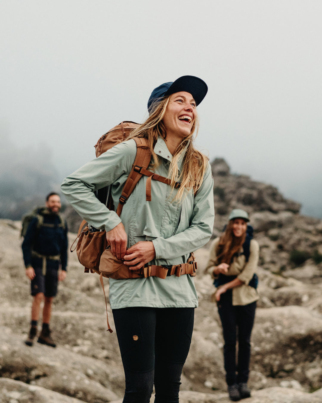 Woman hiking on a rocky mountain with a backpack, smiling. photo by fjallraven