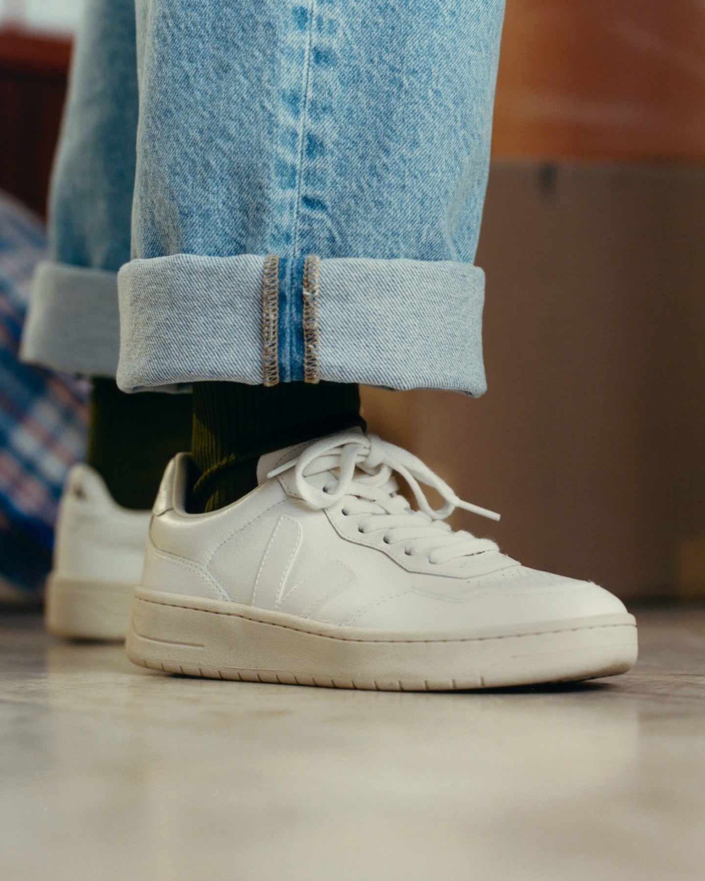 White sneakers worn with rolled-up jeans on a blurred background photo by Veja