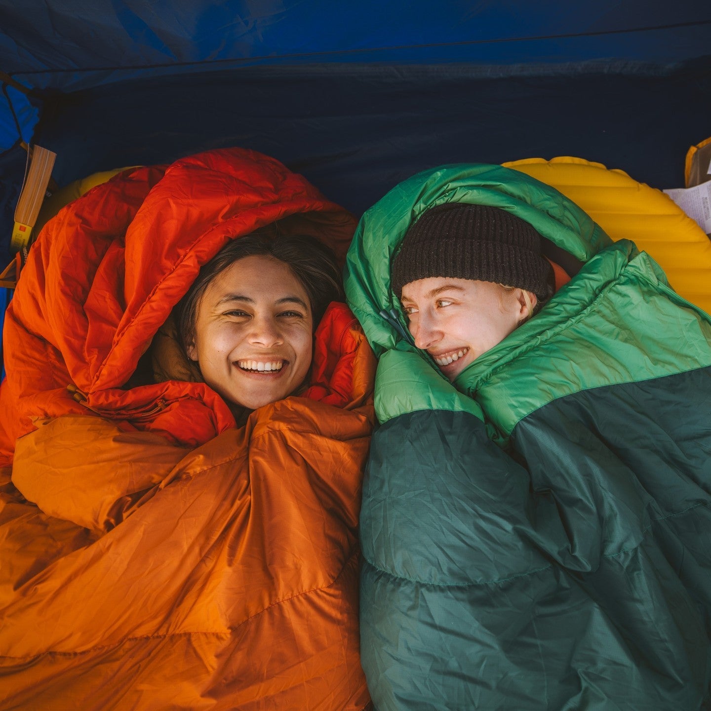 Two people in orange and green sleeping bags inside a tent photo by Marmot