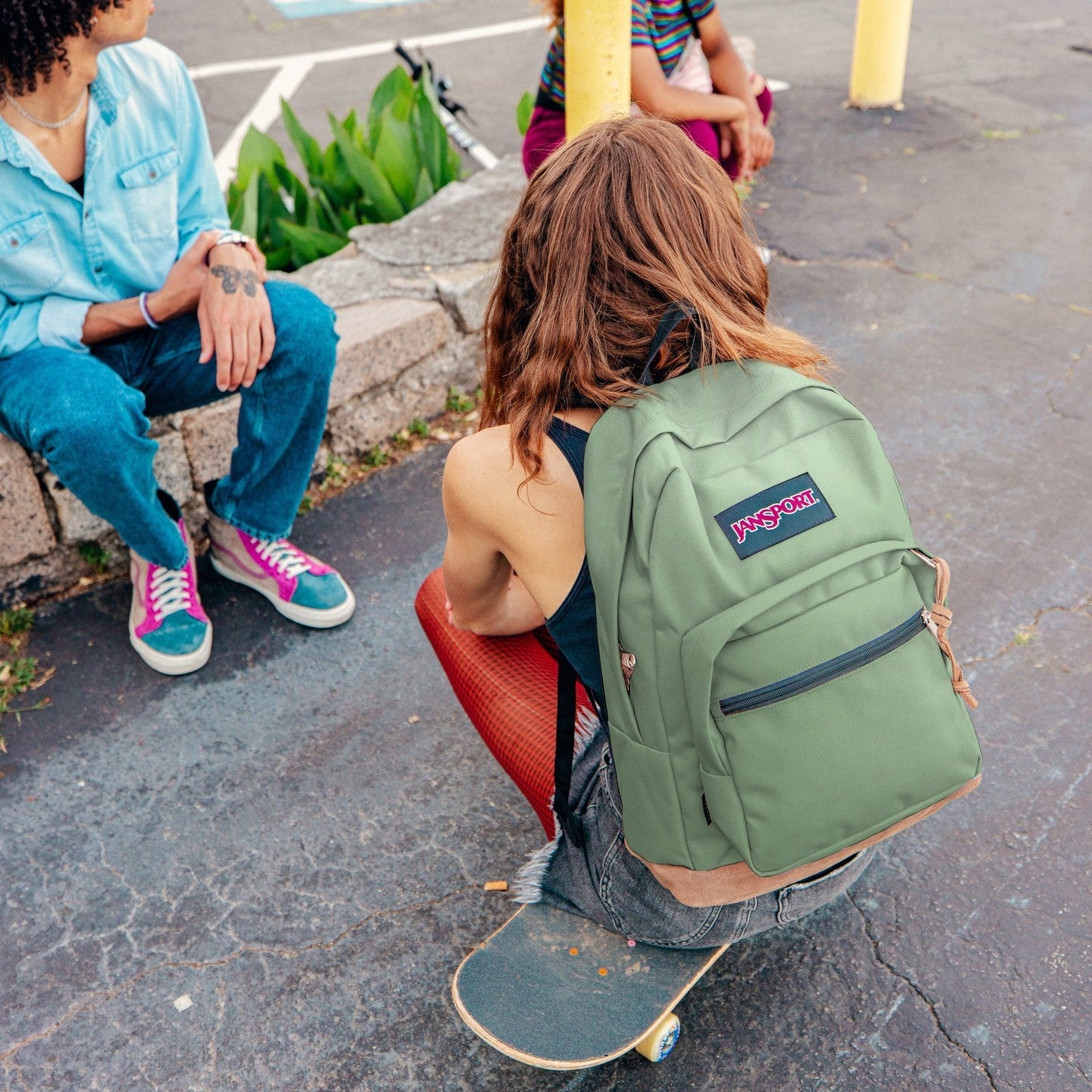 Person with a green backpack sitting on a skateboard in an urban setting photo by Jansport