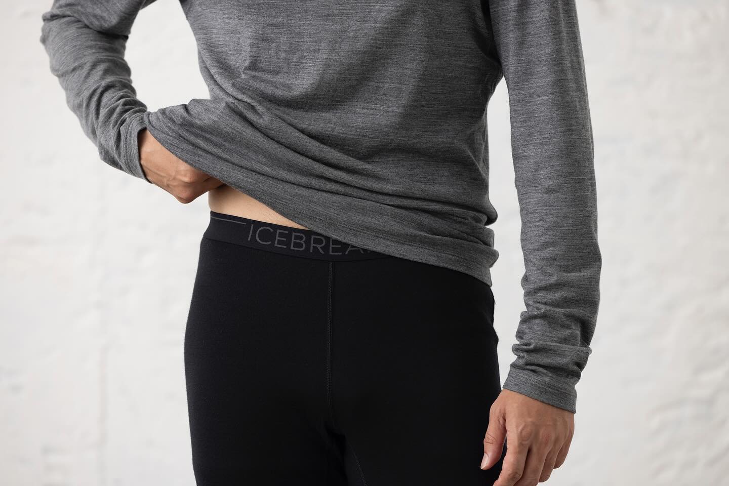 Person wearing a gray baselayer shirt and black baselayer bottoms with Icebreaker branding on a light background