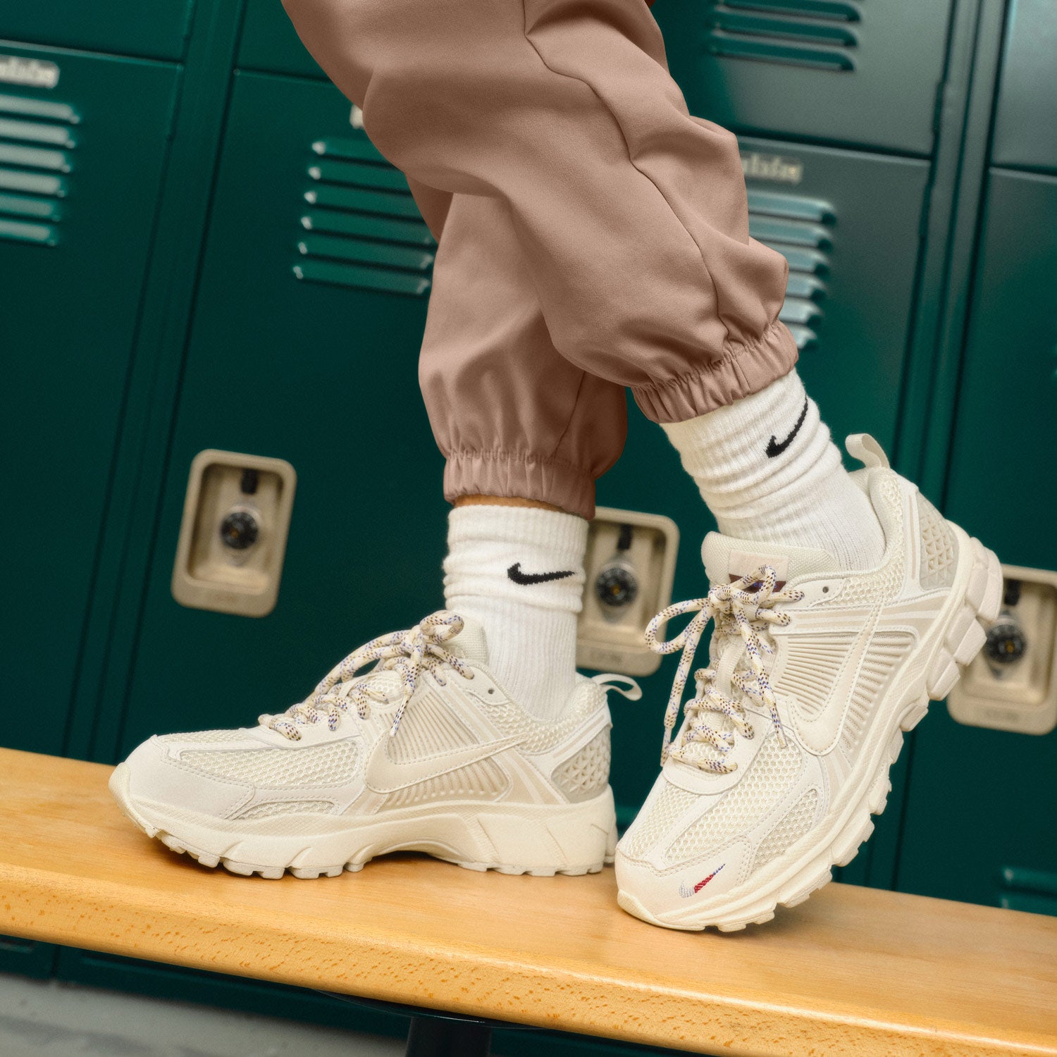 kid wearing beige sneakers and brown pants standing on a wooden bench in a locker room photo by: nike